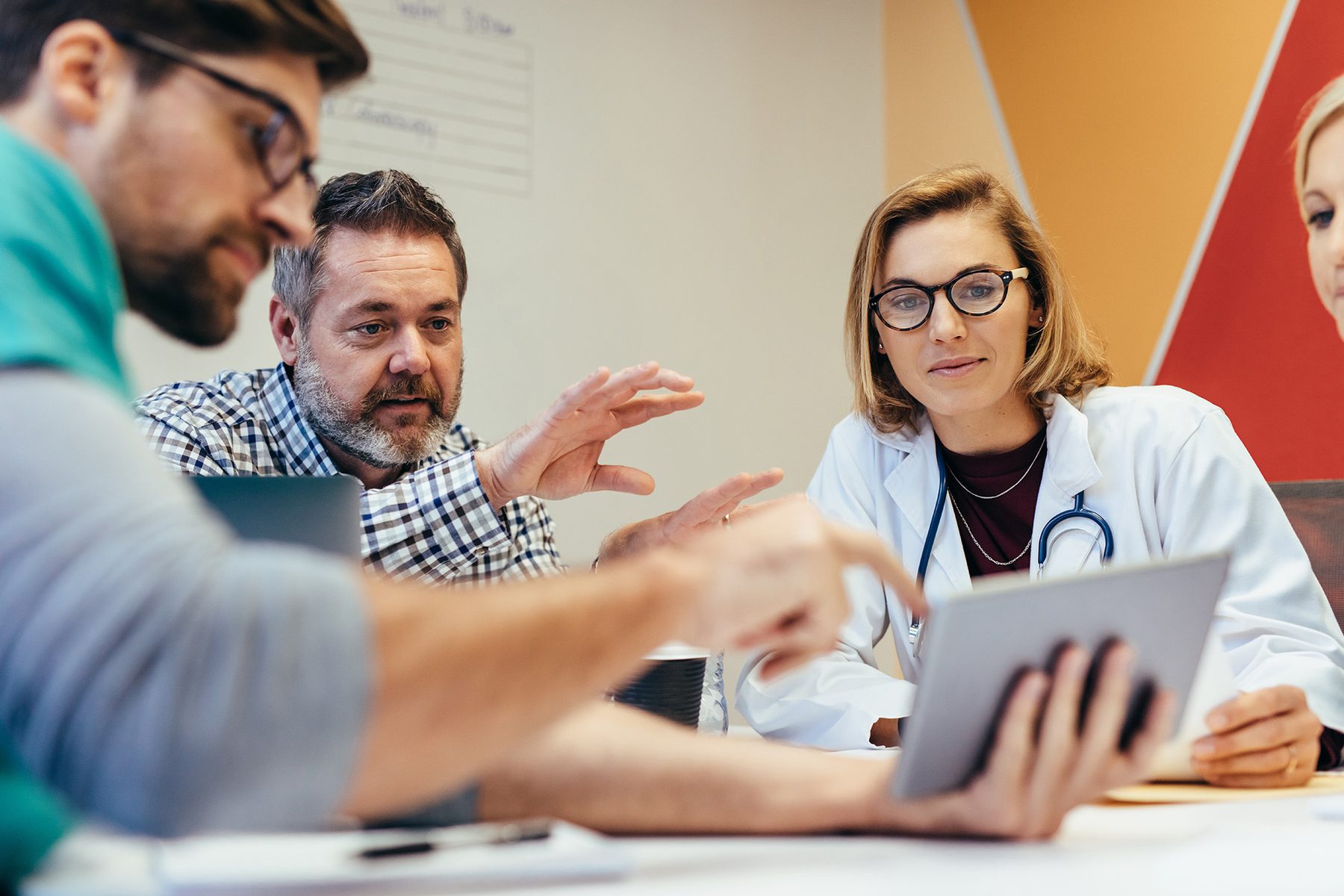 A clinician and colleagues around a meeting table looking at figures on a tablet